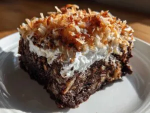 A moist slice of German Chocolate Poke Cake topped with whipped cream and toasted coconut flakes.