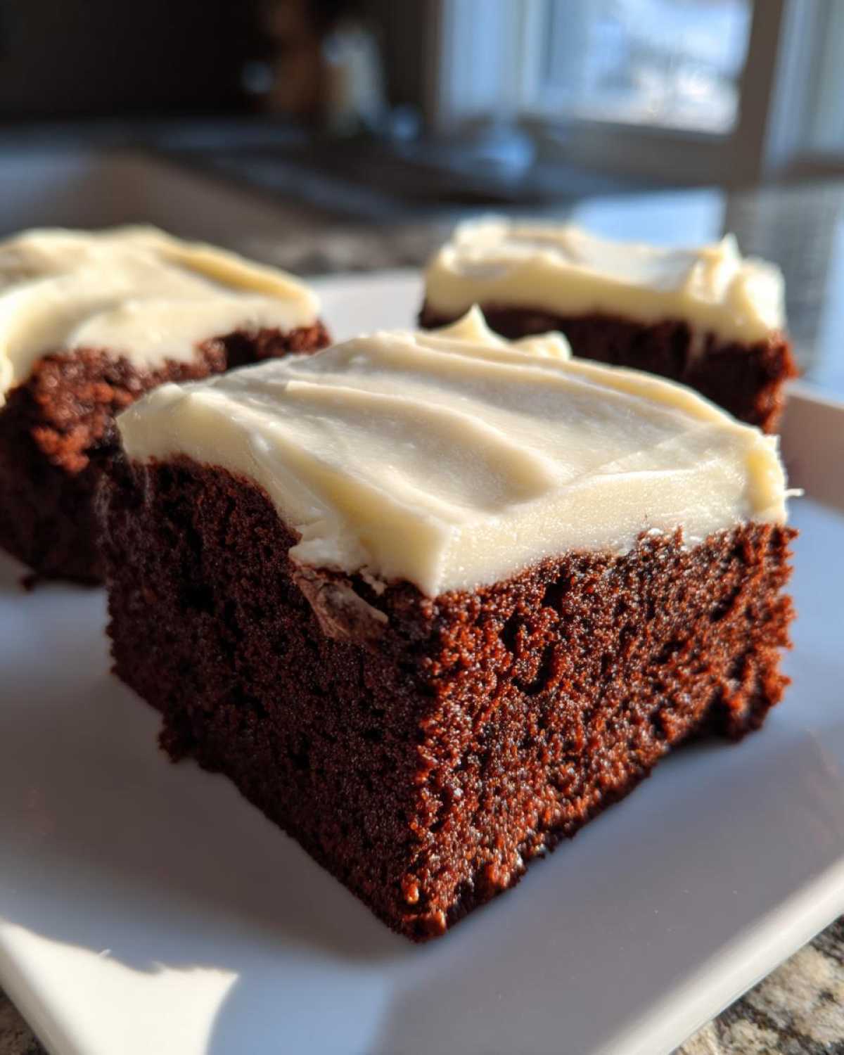 Close-up of three rich, dark gingerbread brownies topped with thick white cream cheese frosting.