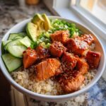 A close-up of delicious salmon bowls featuring glazed salmon cubes over brown rice with avocado and cucumber slices.