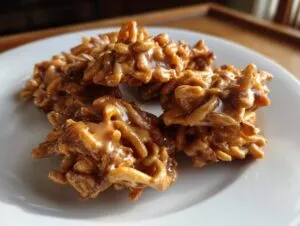A cluster of freshly made, gooey caramel haystack cookies piled on a white plate.