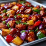 Close-up of sticky, glazed hawaiian chicken sheet pan pieces mixed with pineapple, red onion, and bell peppers.