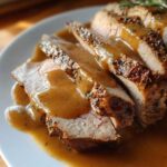 Close-up of sliced instant pot turkey breast covered in rich brown gravy on a white plate.