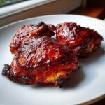 Three pieces of incredibly juicy bbq chicken thighs covered in a thick, glossy, dark red barbecue sauce.
