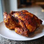 A whole, beautifully roasted spatchcock chicken with crispy, dark golden-brown skin resting on a white plate.