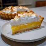 Close-up of a slice of lemon meringue pie showing thick, bright yellow filling and toasted meringue peaks.