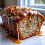 Close-up of a slice of moist apple dapple cake topped with a thick, dripping caramel glaze.