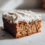 Close-up of a moist slice of applesauce cake topped with thick, creamy white frosting.
