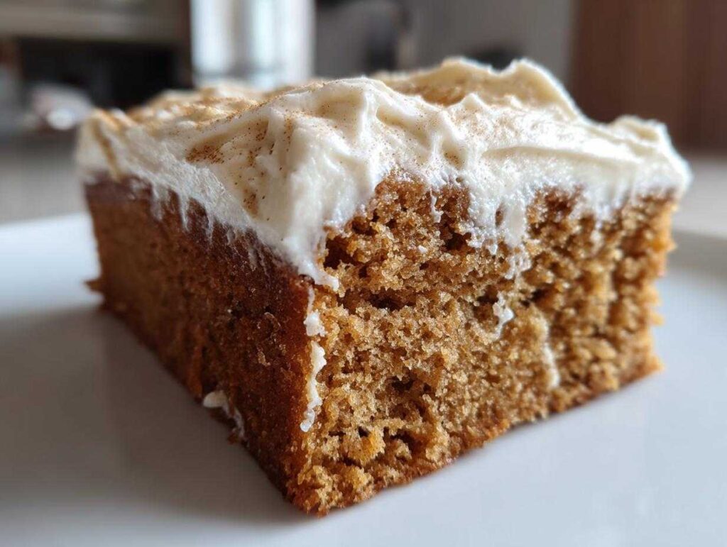 Close-up of a moist slice of applesauce cake topped with thick cream cheese frosting dusted with cinnamon.