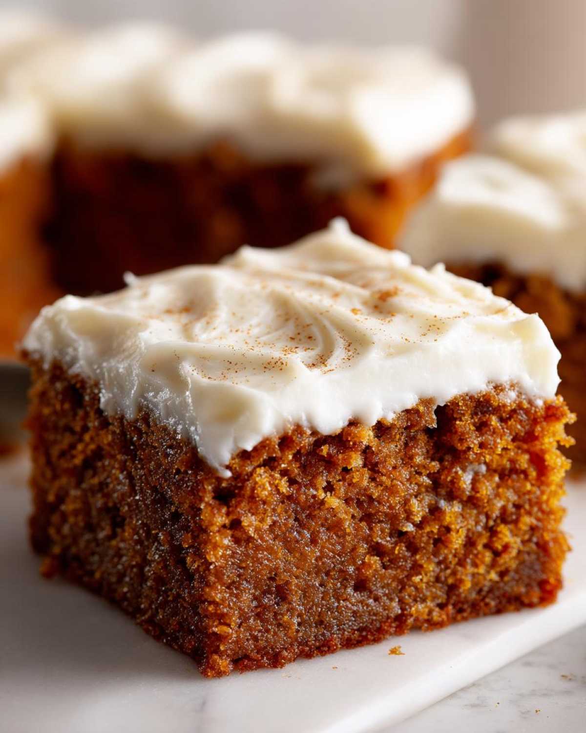 Close-up of a moist slice of applesauce cake topped with thick, white cream cheese frosting and a sprinkle of cinnamon.