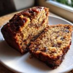 Two thick slices of moist date nut bread showing rich texture, dates, and nuts, served on a white plate.