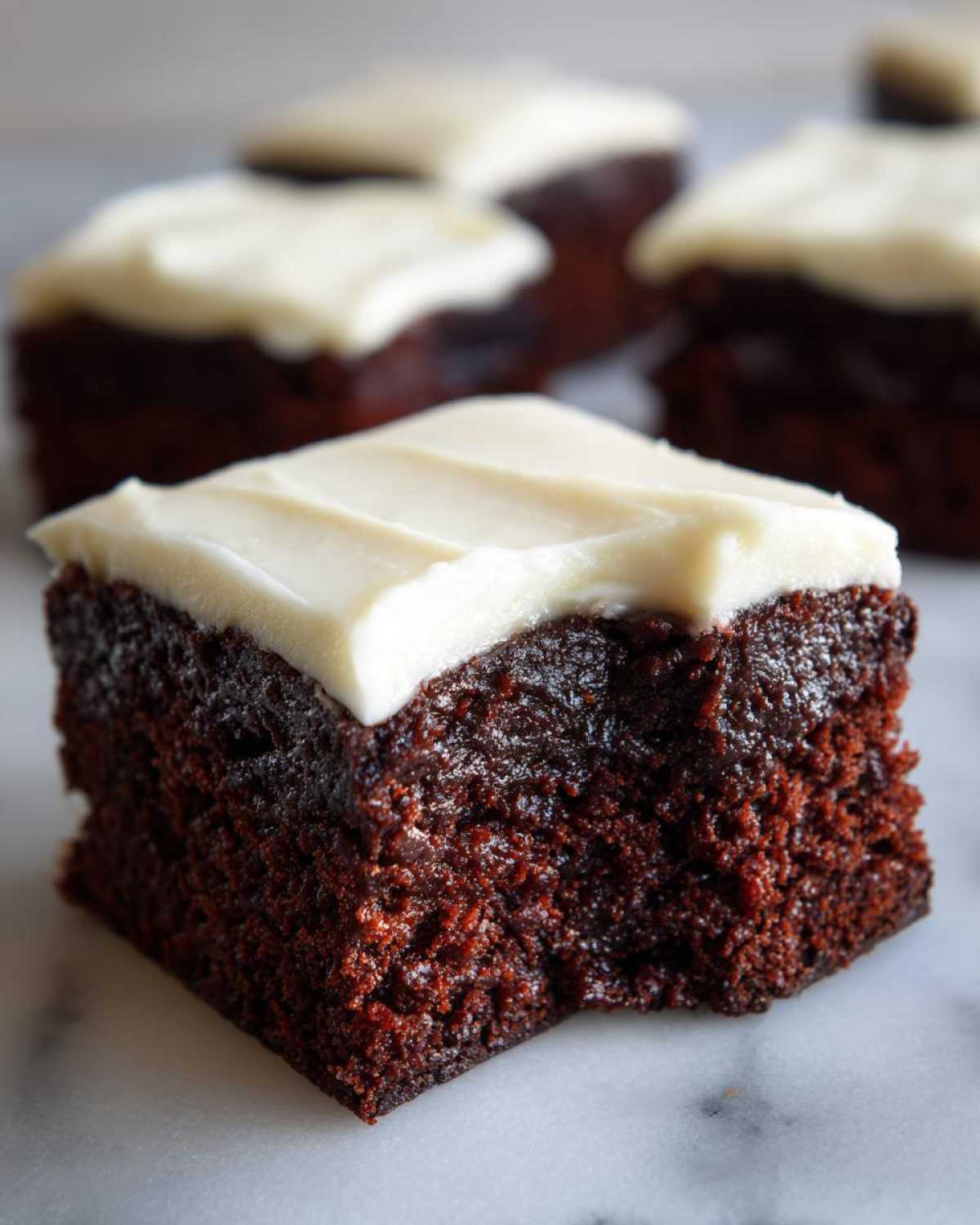 Close-up of a square gingerbread brownies piece with thick white frosting and a small bite taken out.