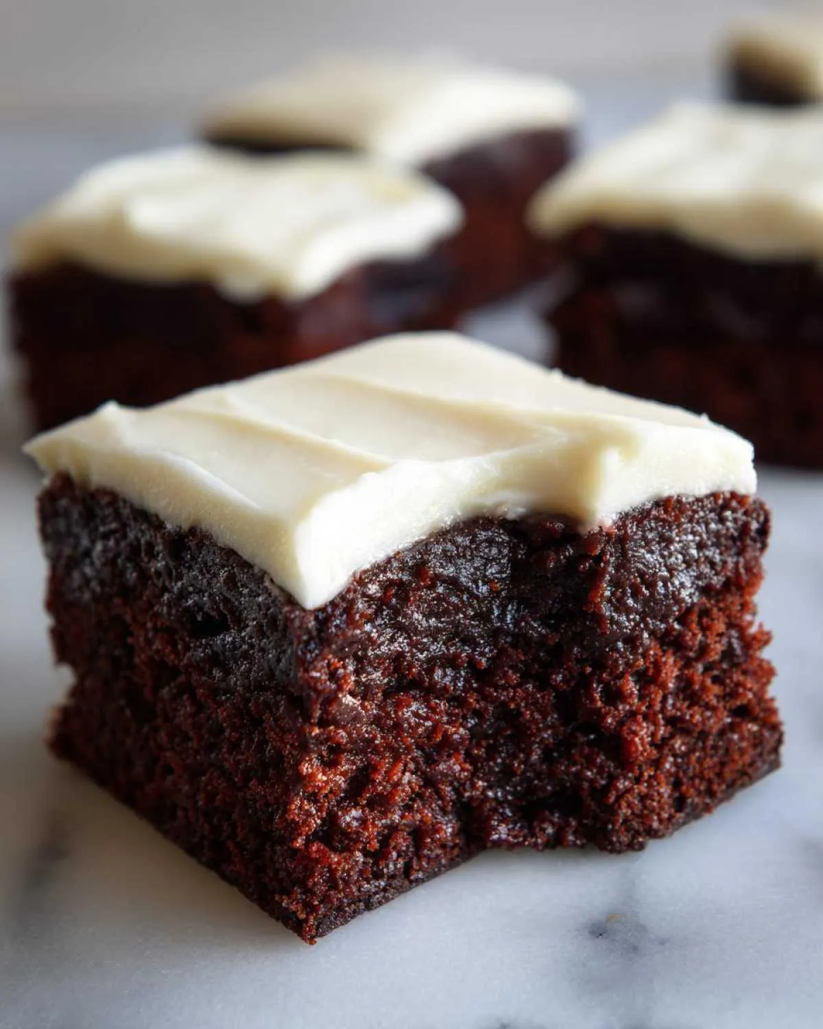 Close-up of a square gingerbread brownies piece with thick white frosting and a small bite taken out.