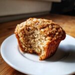 Close-up of a moist oatmeal muffin with a bite taken out, showing its soft texture and oat topping.