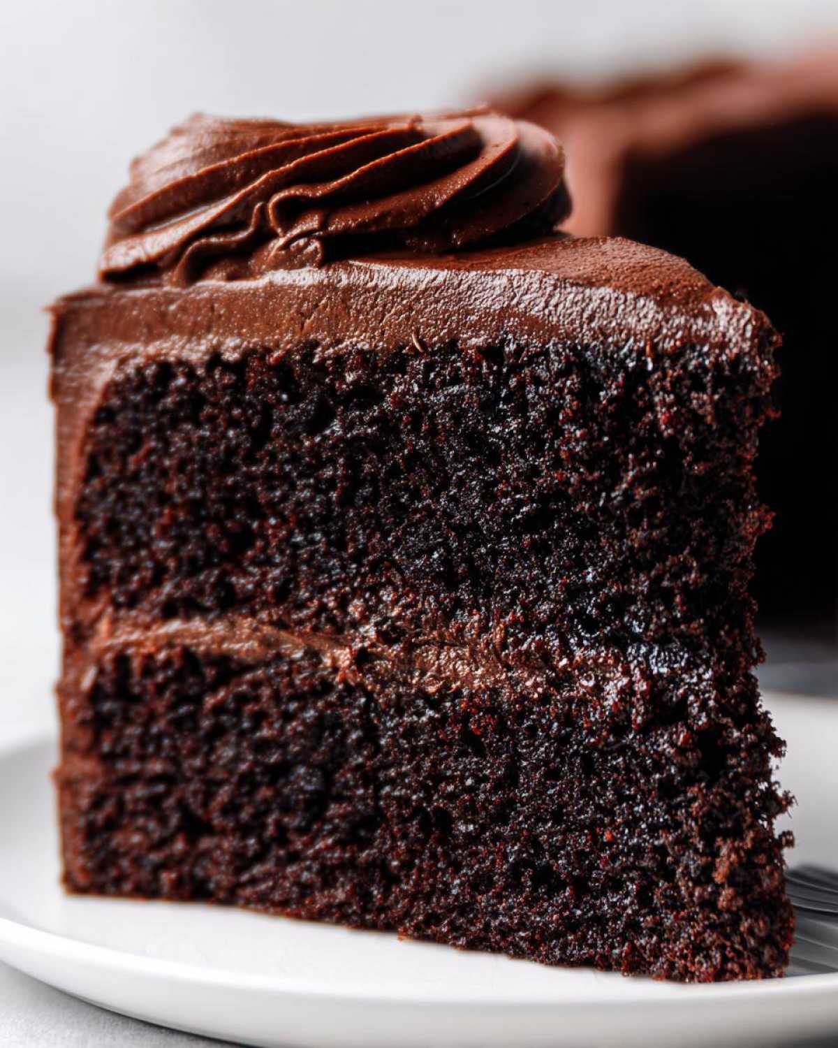 Close-up of a moist slice of dark chocolate cake with thick chocolate frosting, part of our chocolate cake recipe.