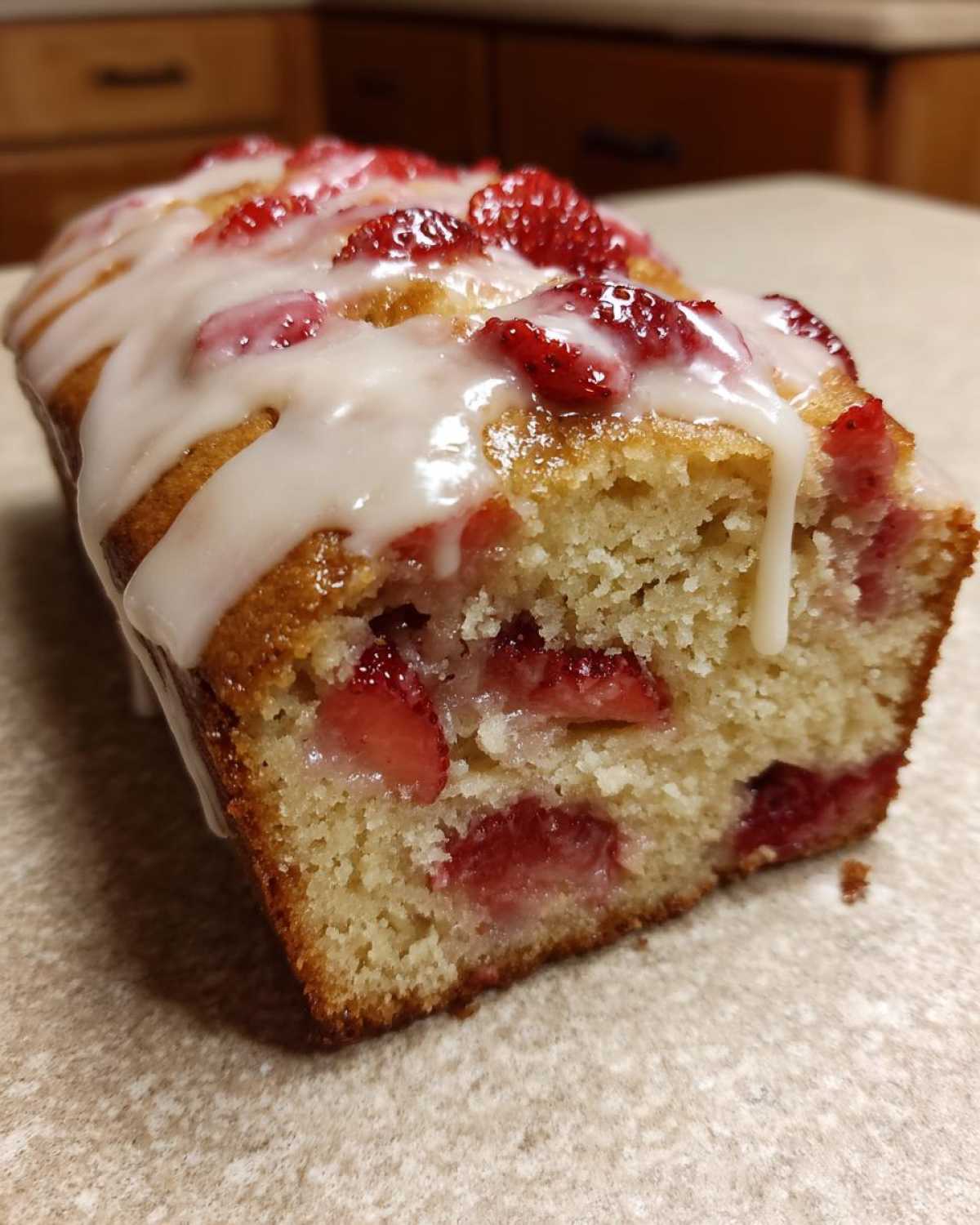 Close-up of a moist strawberry bread loaf slice topped with white glaze and fresh strawberry pieces.