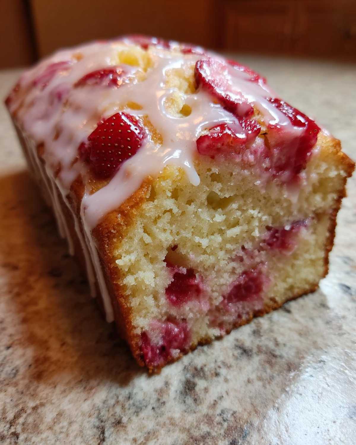Close-up of a moist strawberry bread loaf, showing the crumb texture and sliced strawberries topped with a sweet white glaze.