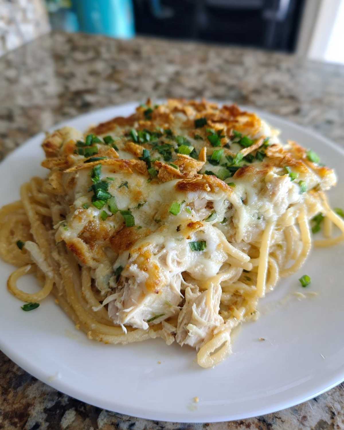 A close-up serving of Monterey chicken spaghetti topped with melted cheese, crispy onions, and fresh green onions.