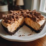A slice cut from a no-bake butterfinger pie showing a thick, creamy filling and chocolate crust, topped with crushed Butterfinger pieces.