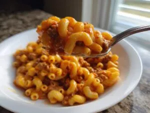 A spoonful of creamy, cheesy taco pasta with ground meat being lifted from a white bowl.