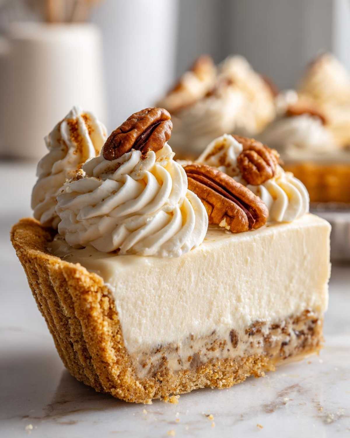 Close-up of a slice of pecan cream pie featuring a thick, creamy filling, graham cracker crust, and whipped cream topped with pecans.