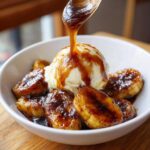 A scoop of vanilla ice cream topped with caramelized bananas and rich sauce being poured over it for amazing bananas foster.