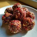 A cluster of homemade goat cheese balls coated in a vibrant red, crunchy nut and spice mixture.