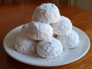 A stack of delicious Russian tea cakes heavily coated in powdered sugar, resting on a white plate.