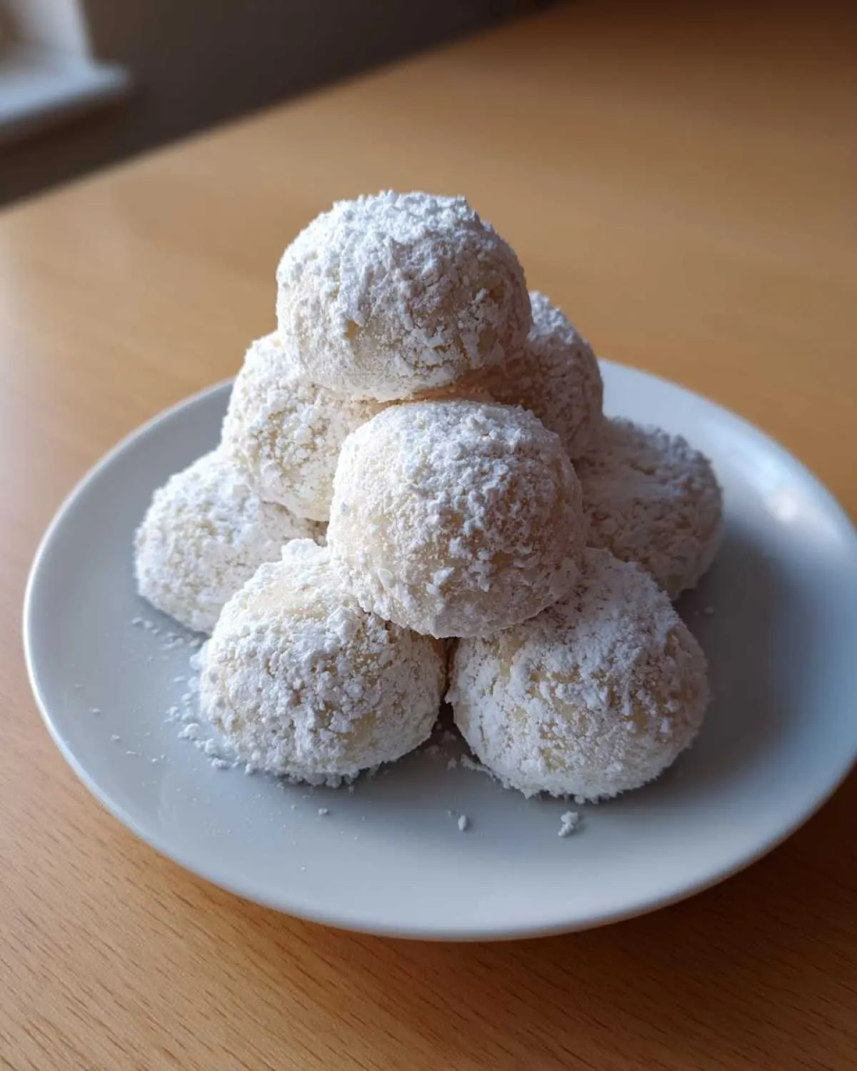 A mound of freshly baked Russian tea cakes heavily dusted with powdered sugar, resting on a light gray plate.