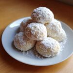 A small stack of freshly baked russian tea cakes heavily dusted with powdered sugar on a white plate.