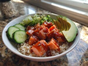 A close-up view of a vibrant salmon bowls featuring glazed salmon chunks over brown rice, topped with sliced avocado and cucumber.