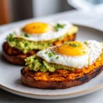 Two slices of savory sweet potato toast topped with mashed avocado and a sunny-side-up egg.