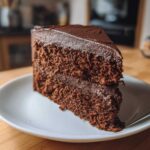 A rich slice of dark chocolate cake topped with thick, glossy chocolate frosting.