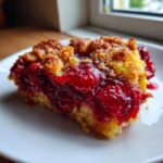 Close-up of a moist slice of cherry dump cake showing bright red cherry filling and golden crumb topping.
