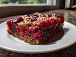 A close-up of a square slice of moist cherry dump cake with a golden crust, served on a white plate.