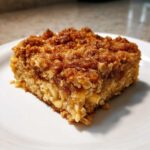 Close-up of a square slice of baked oatmeal with a thick, brown sugar cinnamon crumb topping.