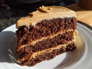 Close-up of a rich, dark slice of gingerbread latte cake with two layers of light brown frosting.