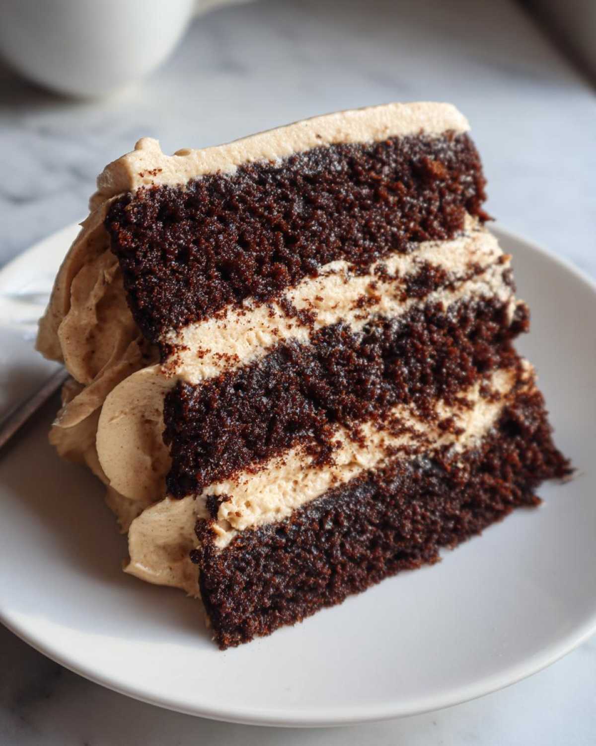 Close-up of a moist slice of dark chocolate gingerbread latte cake layered with light brown coffee-flavored frosting.