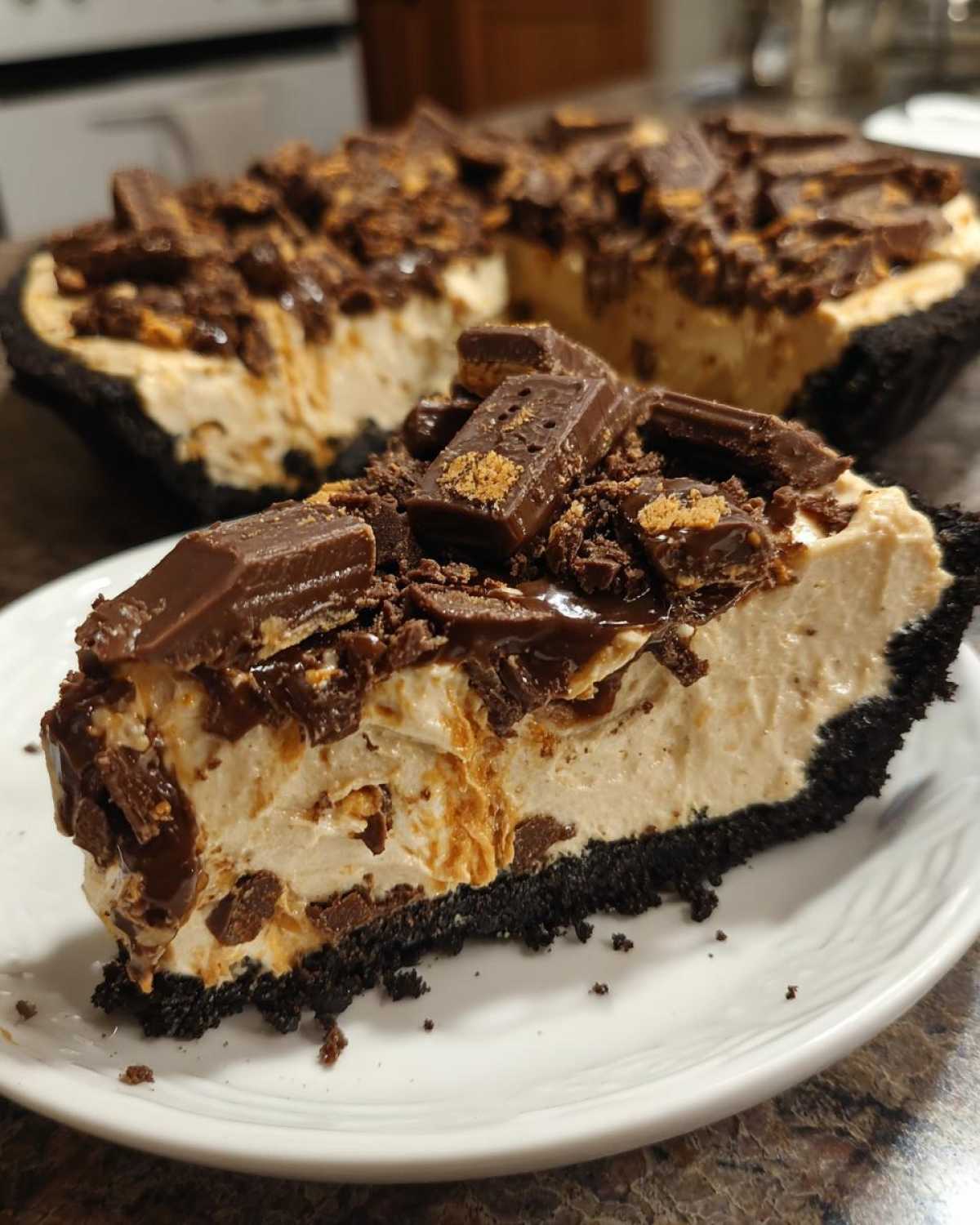 A close-up slice of no-bake butterfinger pie featuring a dark chocolate crust, creamy filling, and topped with chopped Butterfinger pieces.