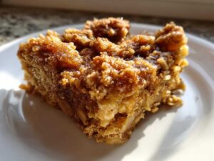 Close-up of a square slice of moist baked oatmeal with a rich, caramelized crumb topping on a white plate.