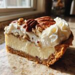 A close-up slice of rich pecan cream pie showing a thick, creamy filling, graham cracker crust, and whipped topping with whole pecans.