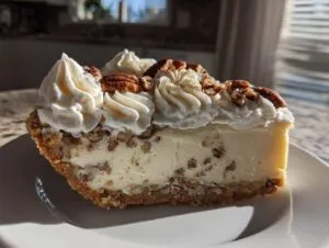 A decadent slice of pecan cream pie featuring a creamy filling, pecan crust, and swirls of whipped cream topped with pecans.