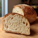 A loaf of soft sourdough sandwich bread sliced in half, showing the open, airy crumb structure.