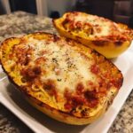 Two halves of baked spaghetti squash lasagna topped with melted cheese and herbs.