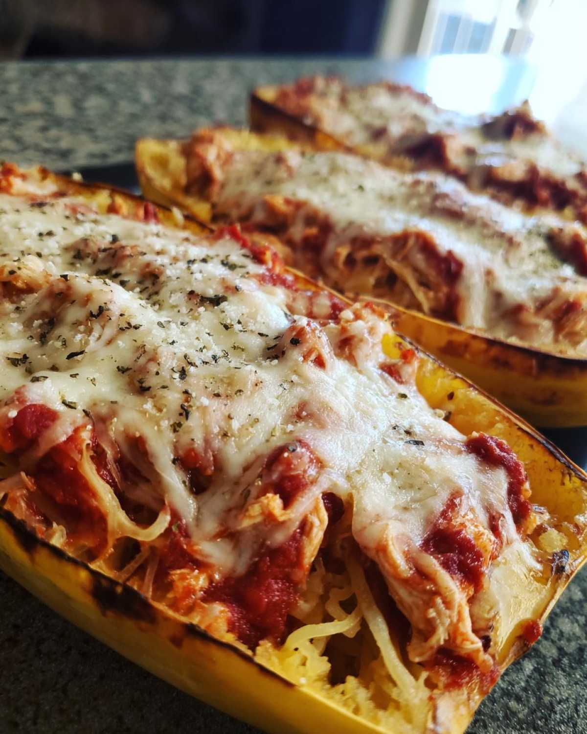 Close-up of baked spaghetti squash lasagna halves topped with melted mozzarella and herbs.