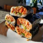 Stack of cut tuna kimbap pieces showing the orange spicy tuna filling, cucumber, and rice wrapped in dark nori seaweed.