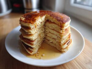 A tall stack of fluffy almond flour pancakes, cut to show the interior texture, drizzled with syrup.