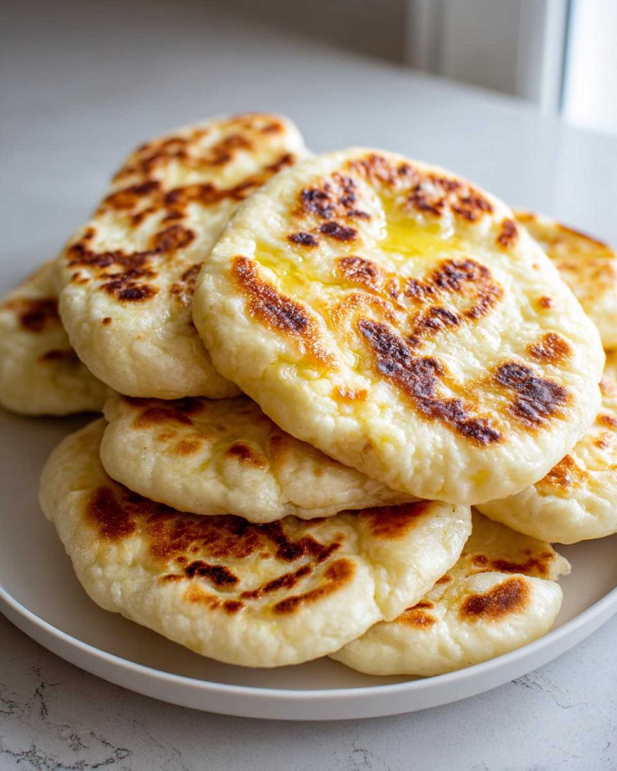 A stack of fluffy, freshly cooked naan bread pieces, lightly browned and brushed with melted butter.