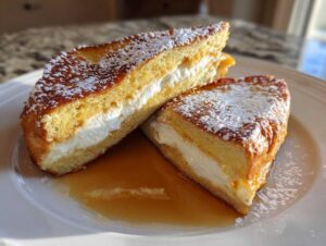 Two halves of golden brown stuffed french toast filled with cream cheese, dusted with powdered sugar, sitting in syrup.