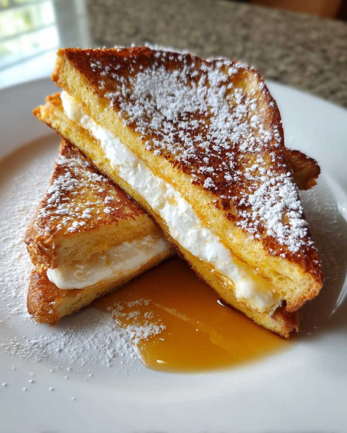 Two halves of cream cheese stuffed french toast stacked, dusted with powdered sugar and drizzled with syrup.