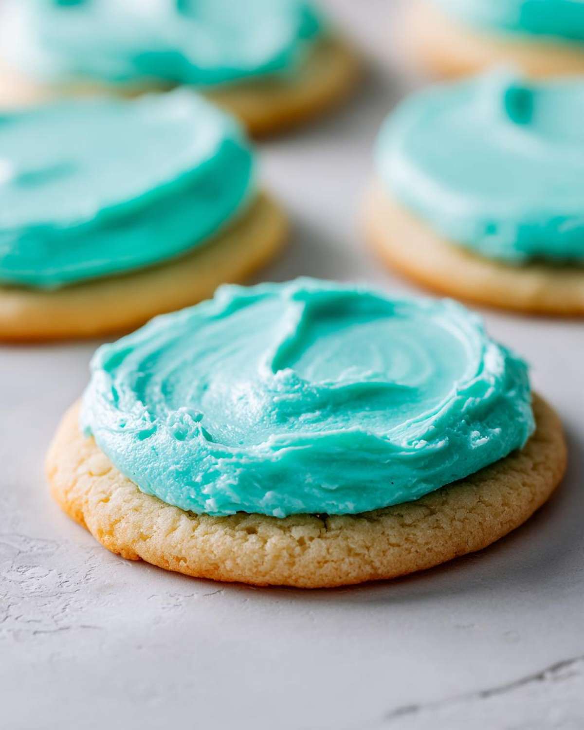 A close-up of a sugar cookie topped with thick, bright turquoise sugar cookie icing recipe frosting.